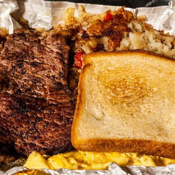 Grilled steak, hash browns, scrambled eggs, and toast served in aluminum foil.