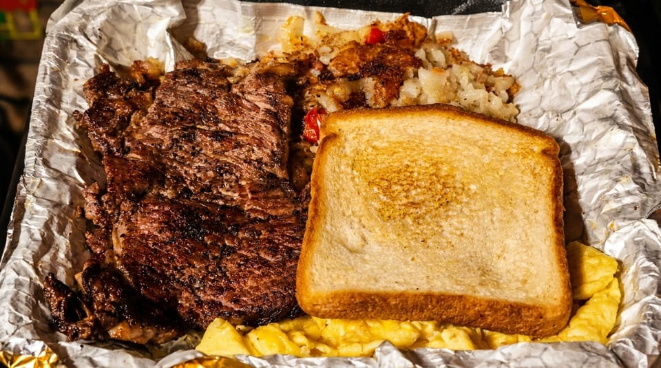 Grilled steak, hash browns, scrambled eggs, and toast served in aluminum foil.