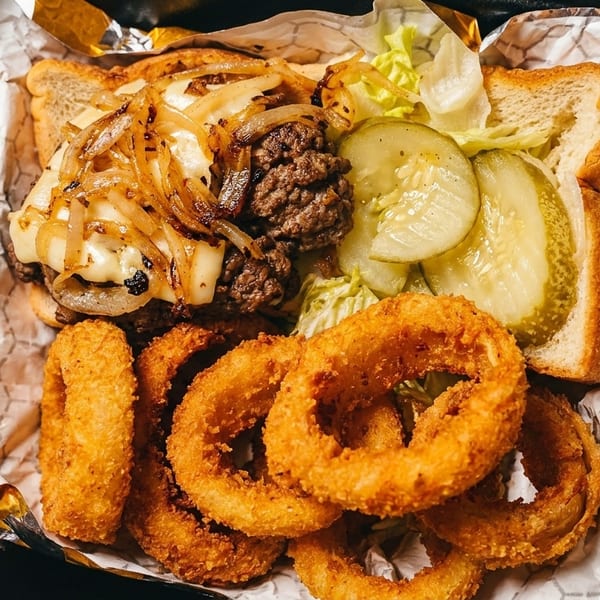 A patty melt with caramelized onions, pickles, lettuce, and a side of crispy onion rings.
